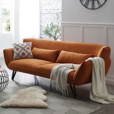 a living room with an orange couch and white rugs on the floor next to a clock