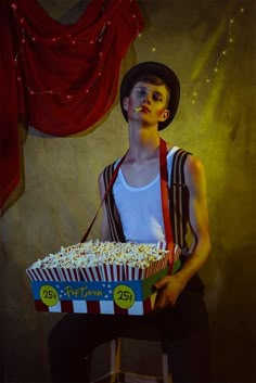 a young man sitting in front of a box of popcorn