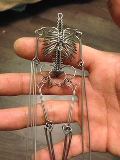 a hand holding a piece of metal art that looks like a skeleton with long legs