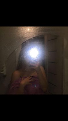 a woman taking a selfie in front of a mirror with a light shining on her face