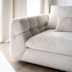 a white couch sitting on top of a hard wood floor next to a curtained window