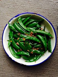 a white bowl filled with green beans on top of a table next to a blue and white plate