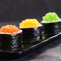 three sushi on a black plate with green, yellow and orange toppings in the middle