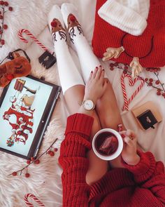 a woman laying on top of a bed holding a cup of coffee next to christmas decorations