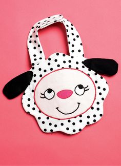 a white and black polka dot bag with a sheep face on the front, sitting on a pink background