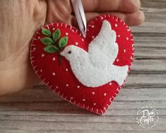 a hand holding a heart shaped ornament with a bird on it