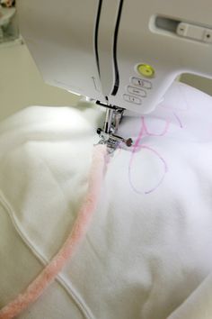 someone is using a sewing machine to sew something on a white pillow with pink writing