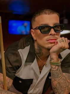 a man with tattoos and sunglasses sitting in front of a pool table