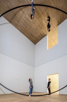 three people standing in an art gallery looking up at the ceiling and hanging upside down