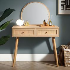 a wooden table with two drawers and a round mirror on the top, in front of a blue wall