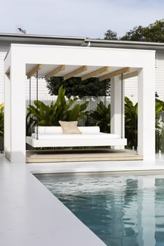 a white bench sitting next to a swimming pool in front of a house with palm trees