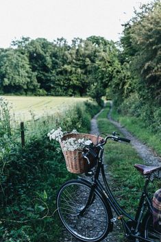 a bicycle parked on the side of a dirt road next to a lush green field