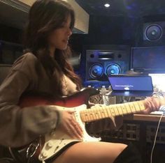 a woman sitting in front of a laptop computer while playing an electric guitar