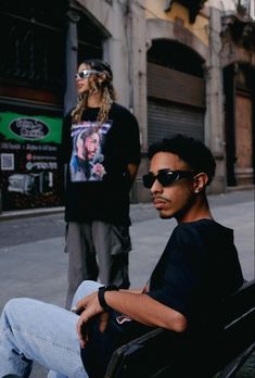 two people sitting on a bench in the middle of an alleyway, one person wearing sunglasses