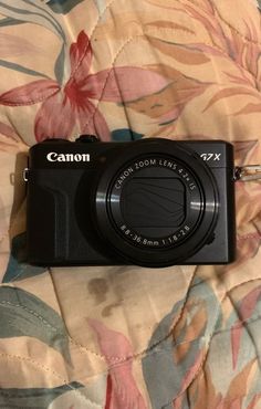 a black camera sitting on top of a flowered bed sheet with the word canon printed on it