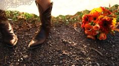 a bride and groom standing next to each other in cowboy boots with their wedding bouquet