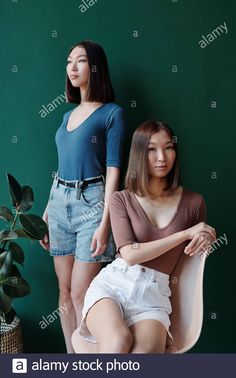 two young women sitting on chairs in front of a green wall