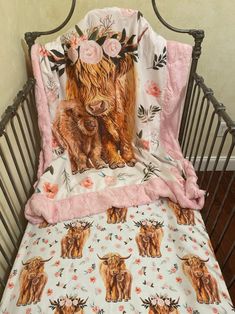 a baby crib with a cow and flowers on it's blanket, next to a pink flowered pillow