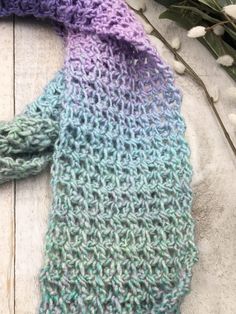 a knitted scarf sitting on top of a wooden table next to flowers and leaves