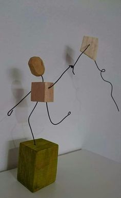 a wooden block with a wire figure standing on it's side and holding onto another piece of wood