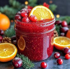 a jar filled with cranberry sauce surrounded by oranges and pine cones