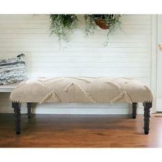 a bench sitting on top of a hard wood floor next to a white wall and potted plants