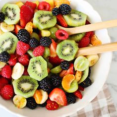 a white bowl filled with cut up kiwis, strawberries and oranges