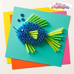 a fish made out of plastic straws sitting on top of some colored paper next to each other