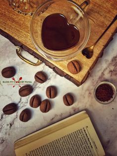 an open book sitting on top of a table next to coffee beans and a glass cup