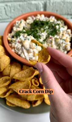 a hand holding a tortilla chip over a bowl of dip next to chips