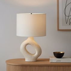 a table lamp sitting on top of a wooden dresser next to a book and bowl