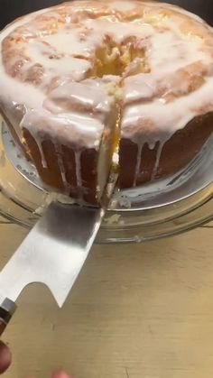 a person cutting into a cake with a knife on a glass platter that is sitting on top of a wooden table