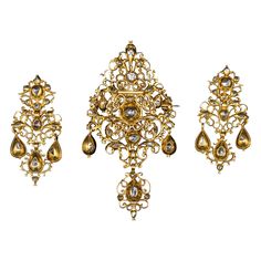 Museum-quality antique late 17th/early 18th century diamond and yellow gold Baroque "sequilé” earrings and pendant/brooch demi-parure, Portuguese, with hallmarks from the period and in the original case. This Georgian sequilé jewel from the first half of the 1700s features intricate filigree, pierced, and die-pressed gold work. It is closed-back set throughout with table-cut and rose-cut diamonds, notable for their almost crude simplicity. The pieces are richly adorned with chiseled and scallope Ornate Baroque Jewelry With Rose Cut Diamonds, Baroque Rose Cut Diamond Gold Jewelry, Baroque Gold Jewelry With Rose Cut Diamonds, Gold Baroque Jewelry With Rose Cut Diamonds, Baroque Rose Cut Diamond Jewelry For Wedding, Antique Ceremonial Jewelry With Rose Cut Diamonds, Ornate Ceremonial Jewelry With Rose Cut Diamonds, Victorian Jewelry With Rose Cut Diamonds For Ceremonial Occasions, Antique Pendant Yellow Gold Earrings