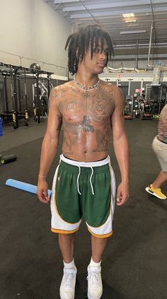 a man with dreadlocks and tattoos standing in a gym wearing green, white and yellow shorts