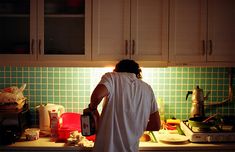 a person standing in a kitchen with green tiles on the wall and counter top, holding a blender