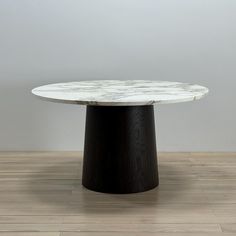 a round marble table with black base on wooden flooring in front of white wall