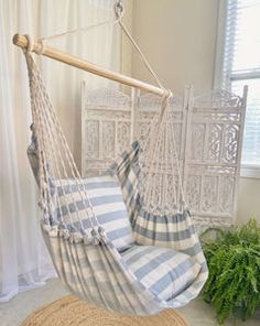 a white and blue striped hammock hanging from a wooden pole in front of a window