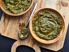 two wooden bowls filled with pesto on top of a cutting board next to spoons