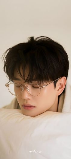 a man with glasses laying on top of a white bed next to a pillow and blanket