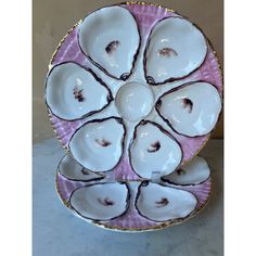 a pink and white plate with gold trimmings on the edge, holding six oysters