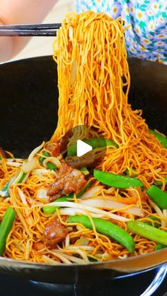 someone stir frying noodles in a wok with chopsticks on the side