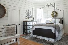 a bedroom with white walls and wood flooring has a black iron bed frame that matches the rug on the hardwood floor