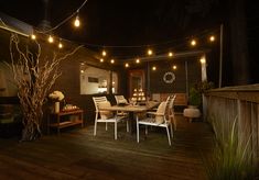 an outdoor dining area with string lights strung over the table and chairs on the deck