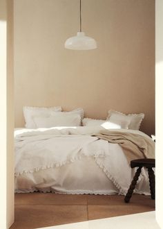 a bed with white linens and pillows in a room that has light colored walls