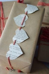 a gift wrapped in brown paper with red string and leaves attached to the wrapping paper