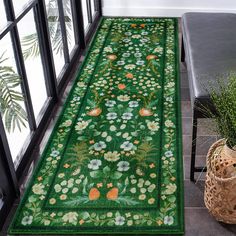 a green rug with flowers on it next to a chair and potted plant in the corner