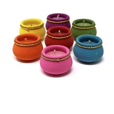 several different colored candles sitting next to each other on a white surface with gold chains around them