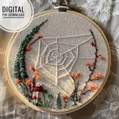 an embroidered spider web with orange flowers and green leaves on a white fabric covered surface