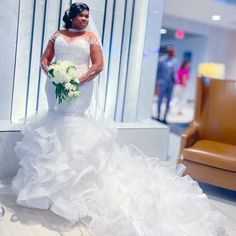 a woman in a wedding dress holding a bouquet and posing for the camera while standing next to a brown chair