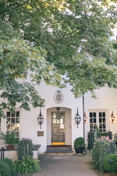 a white house with a clock on the front door and trees in front of it